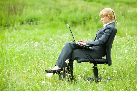 Photo of serious businesswoman sitting on armchair outside and typing on laptop