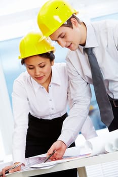Portrait of two architects in helmets discussing document at meeting