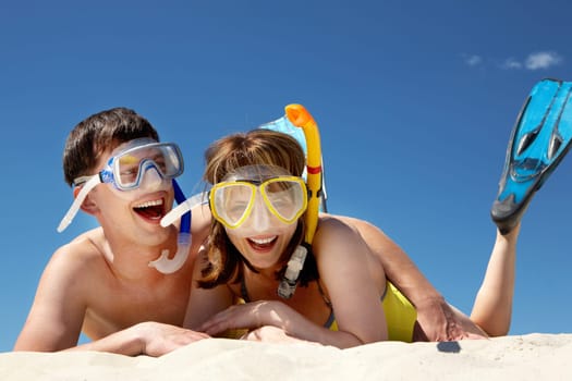 Portrait of cheerful couple in aqualungs lying on sand