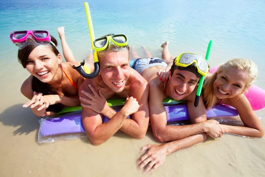 Four friends in scubas lying on sand by water