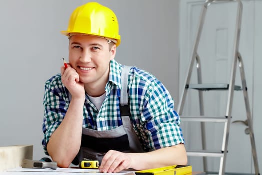 Portrait of a cheerful repairman in helmet sitting at table