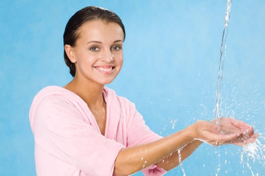 Portrait of happy girl splashing water over blue background and looking at camera