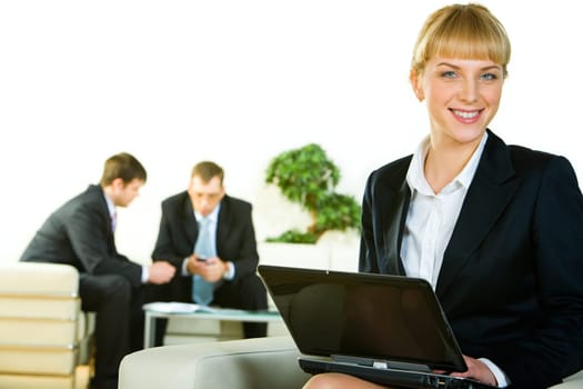 Photo of employee looking at camera and holding the laptop on the background of people working