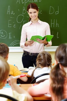Portrait of smart teacher with exercise book looking at schoolkids in classroom