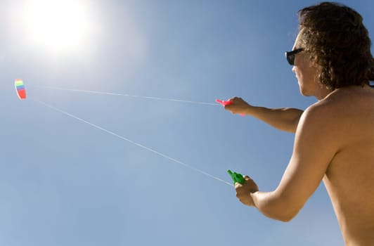 Image of young man flying a colorful kite into bright blue sky with shining sun upwards