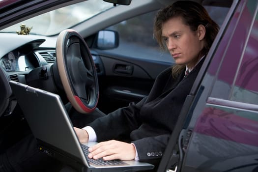 Portrait of serious businessman typing on laptop in the car
