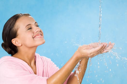 Joyful girl splashing pure water and enjoying it with her eyes closed over blue background