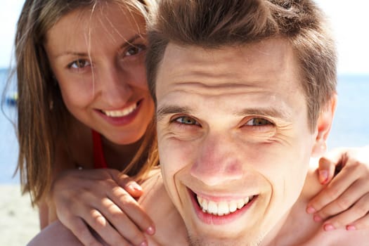 Photo of smiling guy looking at camera while pretty woman behind embracing him