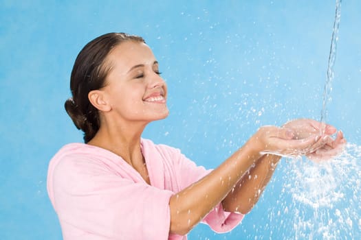 Portrait of happy girl splashing water and enjoying it over blue background