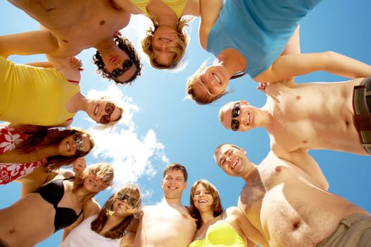 Below view of circle of friends looking at camera with blue sky above them