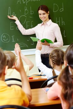 Portrait of smart teacher pointing at blackboard and looking at schoolkids in classroom