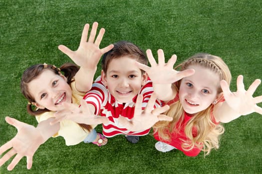 Image of happy friends on the grass raising arms