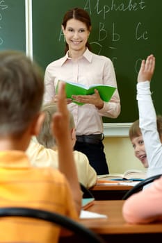 Portrait of smart teacher with exercise book looking at schoolkids in classroom