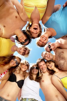 Below view of circle of friends looking at camera with blue sky above them