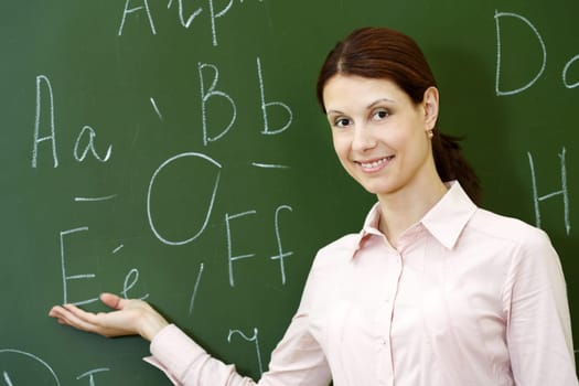 Portrait of smart teacher pointing at letters on blackboard and looking at camera