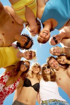 Below view of circle of friends looking at camera with blue sky above them