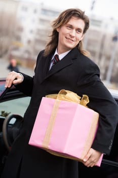 Portrait of attractive young entrepreneur with present in hand somewhere outside
