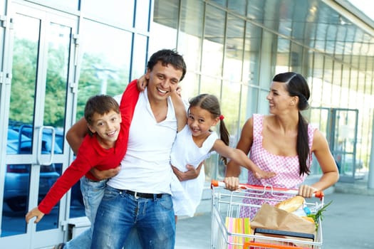 Portrait of happy family of four with cart of foodstuff