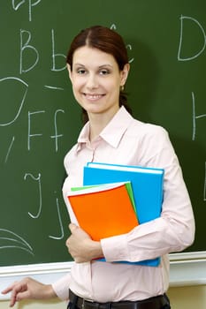 Portrait of smart teacher with books by the blackboard looking at camera