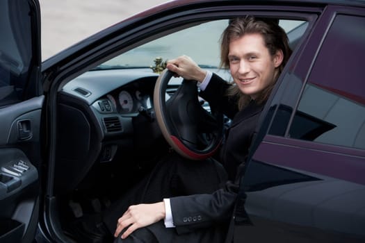 Portrait of cheerful ceo looking out of his automobile and looking at camera with smile