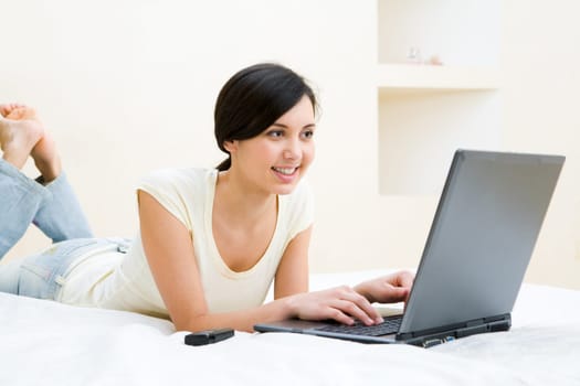 Image of pretty girl looking at laptop monitor while lying on bed in her room