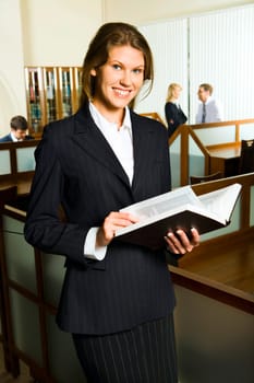 Attractive business woman is holding the book on the background of people in the library