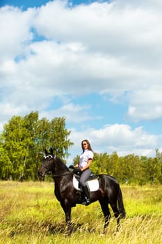 Image of happy female jockey sitting on black horse outdoors