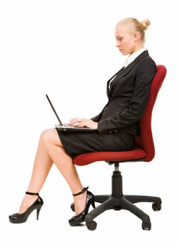 Profile of serious businesswoman sitting on arm-chair and typing on laptop