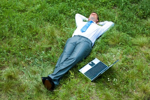 Image of businessman relaxing on the grass with laptop near by