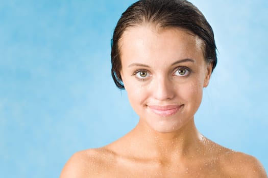 Portrait of pretty girl covered by waterdrops looking at camera over blue background