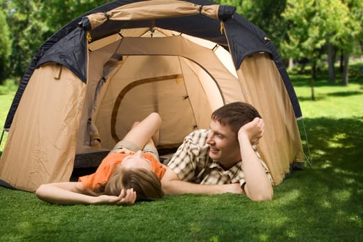 Photo of resting couple lying on green grass in tent and enjoying themselves