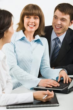 Team of three young businesspeople gathered together around the laptop discussing interesting question