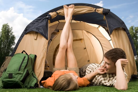 Pretty girl touching boyfriend while lying on grass near tent during summer vacations