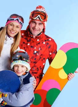 Portrait of happy family with snowboards looking at camera on blue background