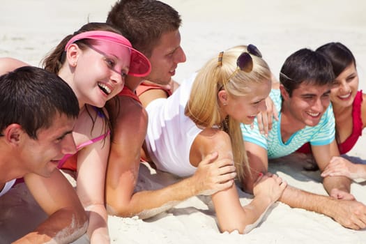 Happy teens lying on sand and posing in front of camera during summer vacation