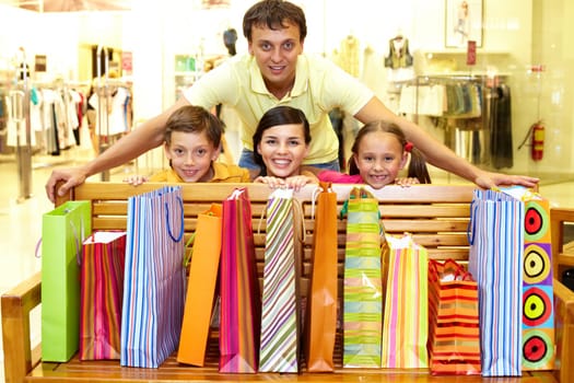 Portrait of a family at bench with plenty of shopping bags looking at camera and smiling