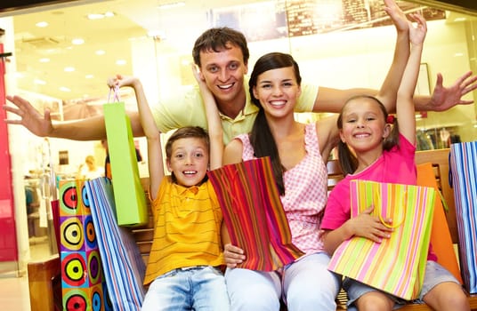 Portrait of joyful family sitting in store with plenty of shopping bags