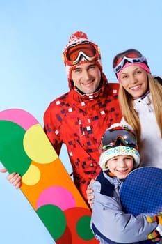 Portrait of happy family with snowboards looking at camera on blue background