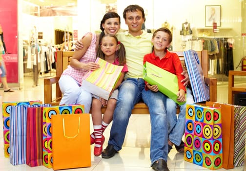 Portrait of a family sitting on bench in store with plenty of shopping bags