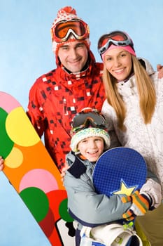 Portrait of happy family with snowboards looking at camera on blue background