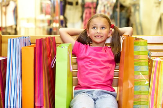 A little girl sitting on bench with plenty of shopping bags