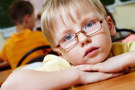 Close-up of schoolboy putting his head on arms and looking at camera