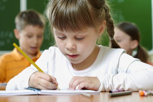 Portrait of smart schoolgirl drawing at lesson in classroom