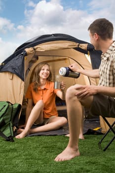 Photo of cheerful girl and guy lying on green grass in tent and looking at camera with smiles
