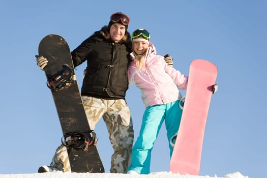 Portrait of joyful man and woman standing on snow with boards in hands