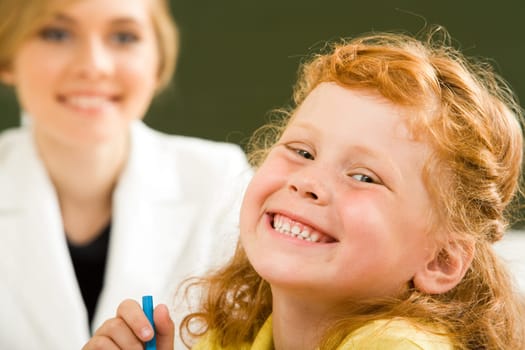 Close-up of happy girl laughing while looking at camera on background of smart teacher