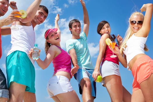 Portrait of happy young friends with cocktails dancing at beach party