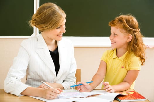 Portrait of teacher and cute schoolgirl sitting at the desk and speaking about lessons