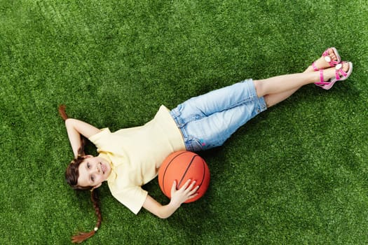 Image of happy girl lying on the grass with ball and looking at camera