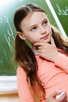 Photo of pensive girl by the blackboard touching her chin while thinking of difficult formula